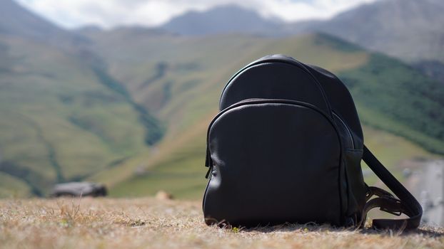 Black backpack on the background of Mount Kazbegi. Traveling in Georgia - Summertime
