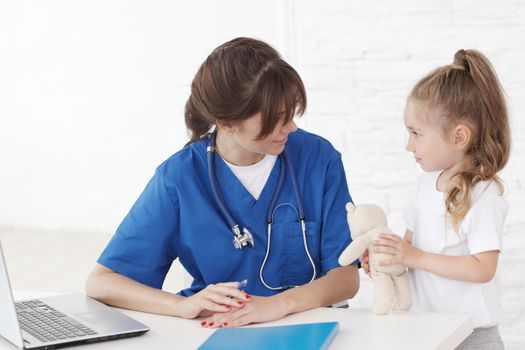 Young smiling female doctor and her little patient with teddy bear