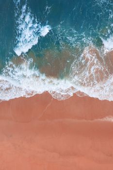Aerial view of pink beach and blue ocean wave.