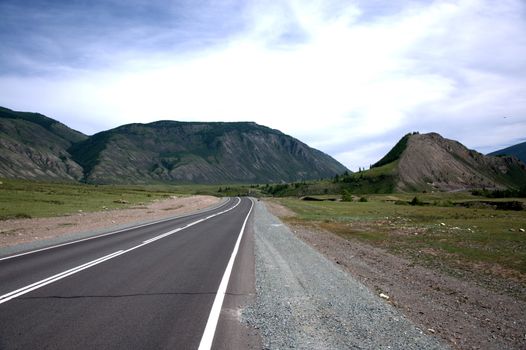 A direct asphalt road running through a valley surrounded by mountains. Altai, Siberia, Russia.