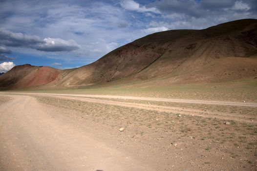 A dirt road going through the steppe at the slope of the Red Mountain. Altai, Siberia, Russia.