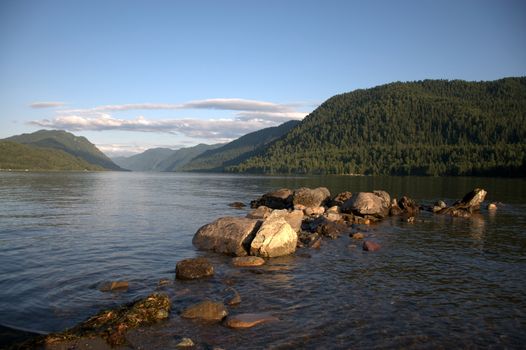 A ridge of stones departs from the coast into the depths of a mountain lake. Teletskoye Lake, Altai, Siberia, Russia.