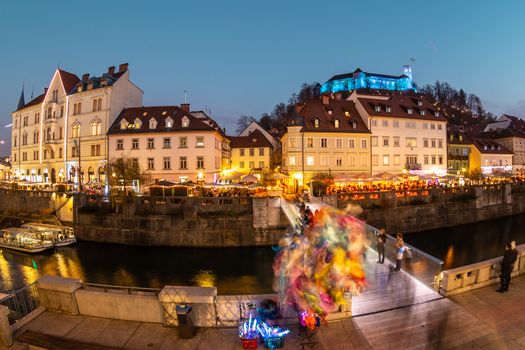 View of lively river Ljubljanica bank in old city center decorated with Christmas lights at dusk. Old medieval Ljubljana cstle on the hill obove the city. Ljubljana, Slovenia, Europe.