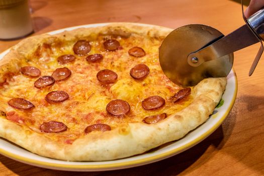 Cutting chorizo sausage pizza with cheese in plate