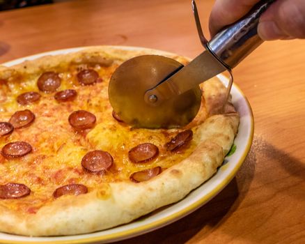 Cutting chorizo sausage pizza with cheese in plate