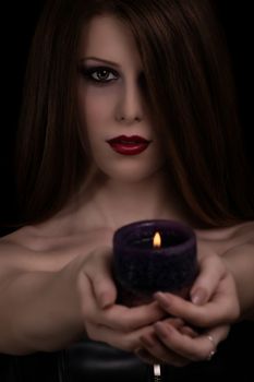 Low key portrait of a mystical beautiful goth girl holding a candle, isolated on black background.