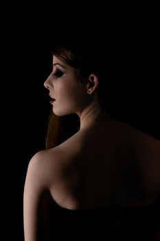 Low key profile shot of a beautiful young girl on black background.