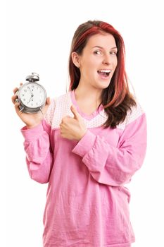 When timing is right. Smiling young girl in pink pajamas holding an alarm clock and giving thumbs up, isolated on white background.