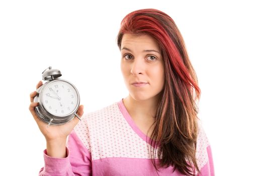 There, I overslept again. What can I do? Confused beautiful young girl in pink pajamas holding an alarm clock, isolated on white background.