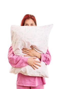 Hiding from the insomnia behind my pillow. Tired and sleepy young girl in pink pajamas hugging a pillow, isolated on white background.