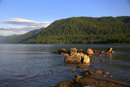 A stone ridge leaving in a mountain lake at sunset. Teletskoye Lake, Altai, Siberia, Altai.