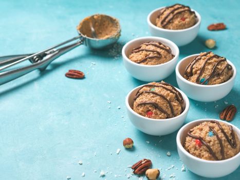 Safe-to-eat raw monster cookie dough in small portion bowl, ice cream scoop and nuts on blue background. Ideas and recipes for kids and toddlers meal. Copy space for text.