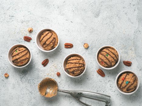 Safe-to-eat raw monster cookie dough in small portion bowl, ice cream scoop and nuts on gray cement background. Ideas and recipes for kids and toddlers meal. Top view or flat-lay. Copy space for text.