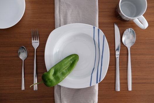 White porcelain tableware with bright metal cutlery and soft napkin on a wooden table.