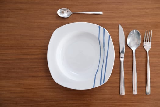 White porcelain tableware with bright metal cutlery and soft napkin on a wooden table.