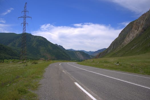 Pole of a high-voltage line on an asphalt road going uphill. Altai, Siberia, Russia.