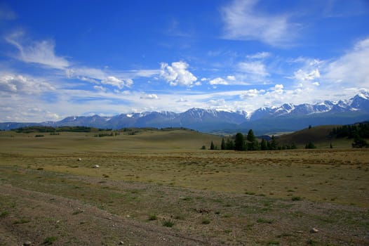 Steppe landscape at the foot of the mountain ranges covered with snow. Altai, Siberia, Russia.