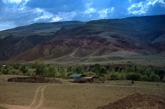A dirt road leading through the steppe to the village at the foot of the Red Mountains. Altai, Siberia, Russia.