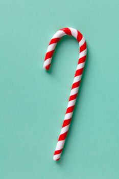 Christmas peppermint candy cane on pastel turquoise background. Festive minimal style flat lay. For greeting card, invitation, social media. Vertical.