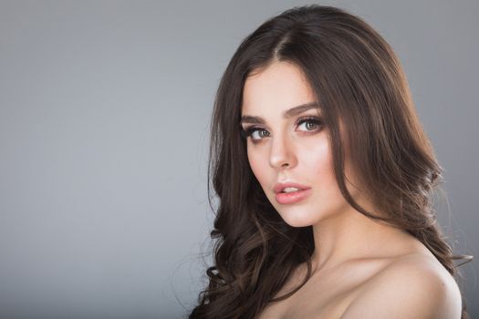 Beauty portrait of young woman with naked shoulder on gray background