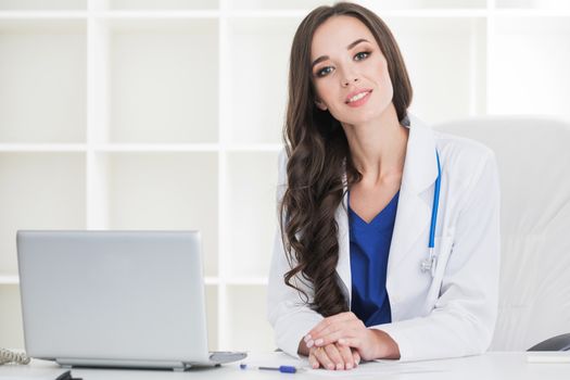 Female doctor working at office desk and smiling at camera , office interior on background