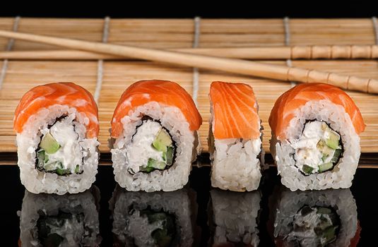 Several Philadelphia Sushi roll in a row. Sushi mat and sticks on a blurry background. Reflection.