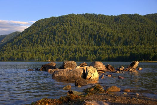 A stone ridge running from the shore to a mountain lake at sunset. Teletskoye Lake, Altai, Siberia, Russia.