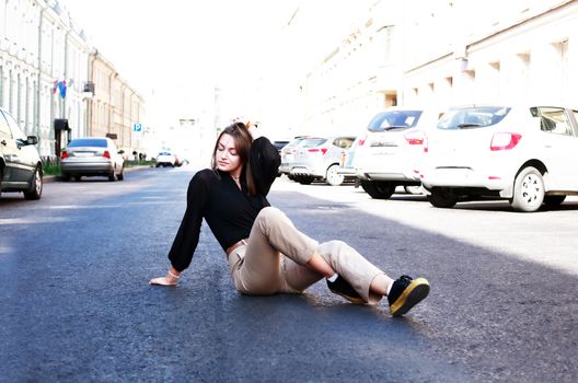 Beautiful young woman sitting on the roadway in the city