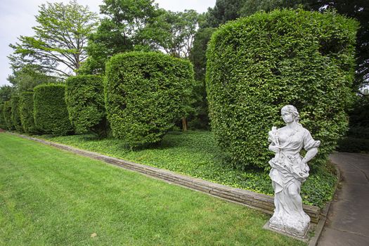 Formal garden with trimmed hedge and a marble statue of woman