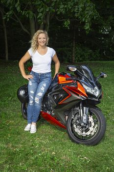 Young woman in jeans and tank top, standing in front of her motocycle