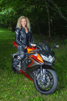 Young blond woman, wearing leather jacket and pants, sitting on her motocycle