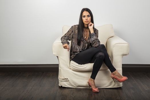 Young brunette woman, wearing stylish clothes, sitting on a white couch