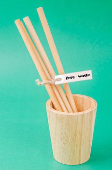 Bamboo drinking straws and wooden glass with Zero - waste on green background, Eco friendly concept.