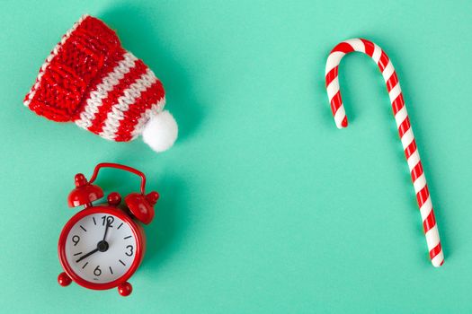 Christmas candy cane, clock and hat on pastel turquoise backdrop with copy space. Winter minimalistic flat lay. Horizontal. Top view. Still life. Waiting for the holiday. Close-up, top view.