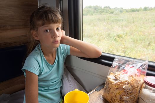 A girl sitting in a reserved seat carriage in a train thoughtfully looks into the frame