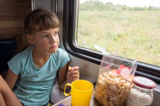 The girl eats cookies on the train and looks out the window
