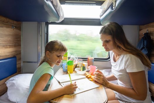 Mom and daughter sit at the table in the train and solve the puzzle in the children's magazine