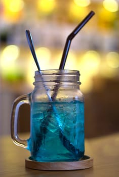 Cold blue cocktail drink, Blue Hawaii Italian Soda or sweetwater and yellow bokeh background in cafe.