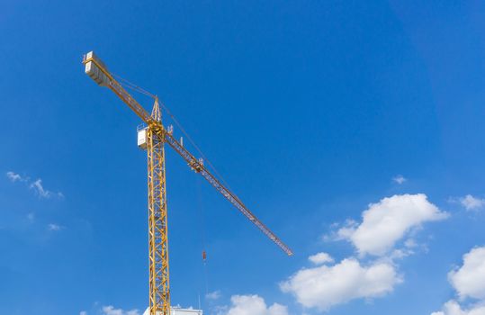 Yellow construction tower crane against blue sky.