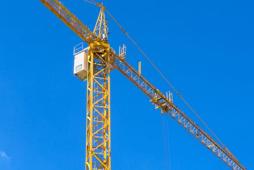 Close up of Yellow construction tower crane against blue sky.