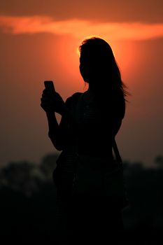 silhouette asian woman touching smartphone at Sunset time.