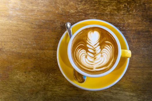 Coffee in yellow coffee cup and on a wood background.