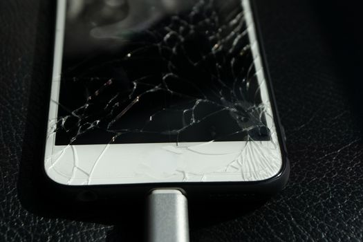 Close up of cracked smartphone screen lay on black leather.