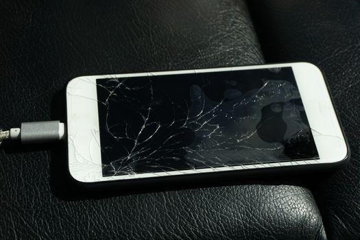 Close up of cracked smartphone screen lay on black leather.