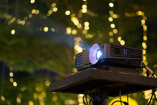 Black Projector on stand table ready for presentation in yellow bokeh background.