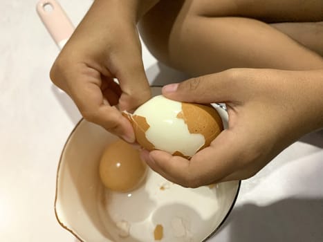 Little Asian boy is peeling boiled egg.