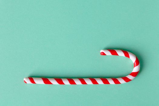 Christmas peppermint candy cane on pastel turquoise background. Festive minimal style flat lay. Mockup with copy space for greeting card, invitation, social media. Horizontal.