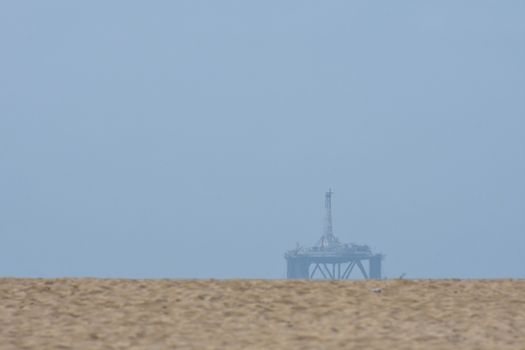 An oil platform at sea visible over beach sand dunes, Mossel Bay, South Africa