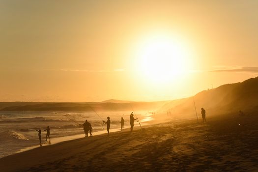 Family vacation with fishing rods on beach at sunset, Mossel Bay, South Africa