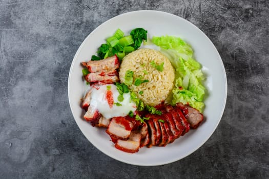 Barbecued red pork and crispy pork in red sauce, served with rice and vegetable on white plate.
